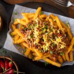 Delicious homemade spicy chili fries with green onion and cheddar cheese.